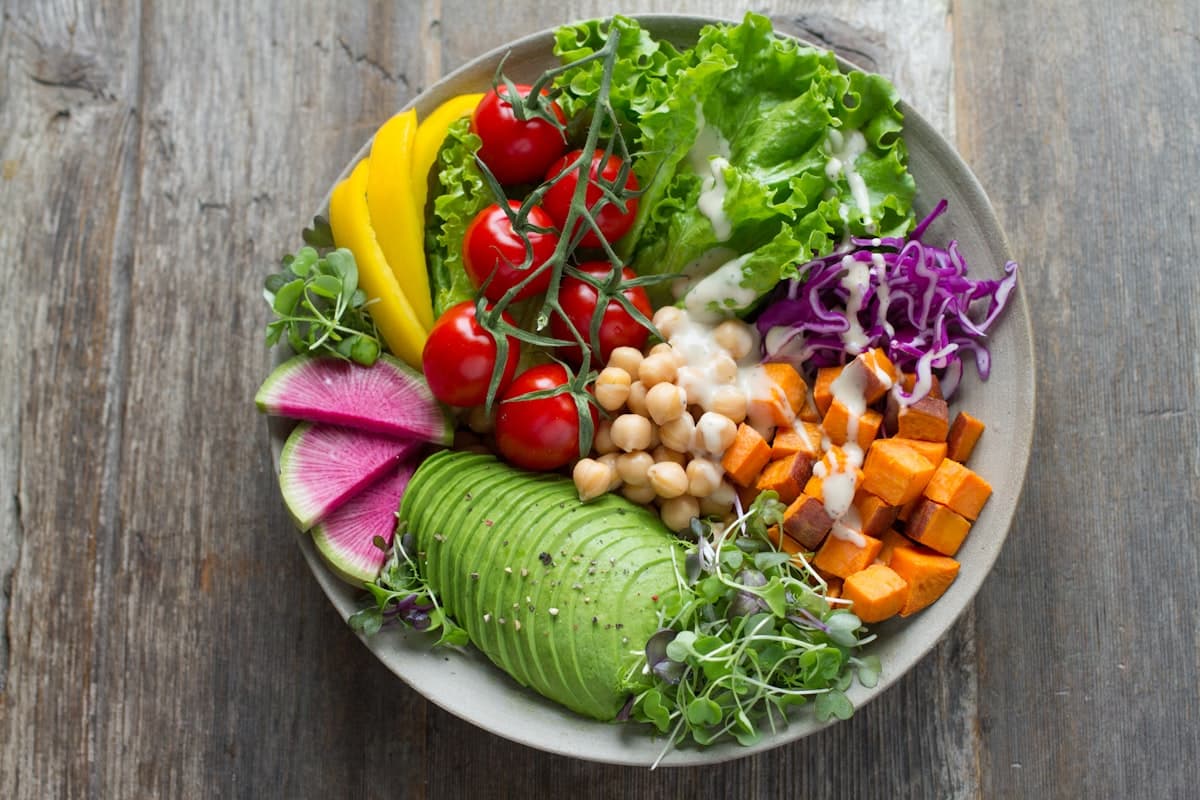 Fresh vegetable bowl with avocado, tomatoes, and greens on a wooden table